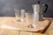 Close-up of two empty glasses with gray coffee pot on brown paper on wooden table, gray background, horizontal