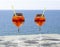 Close up of two glasses of chilled cocktail drinks with straws and ice cubes on a table a sunny day