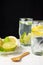 Close-up of two glasses of water with lemon and lime slices with ice cubes on white wood, plate with wooden spoon, half lemons and
