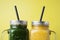 Close up two jars with green and yellow detox smoothie with straws. Spinach and pumpkin smoothie on wooden table