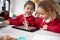 Close up of two kindergarten schoolgirls wearing school uniforms, sitting at a desk in a classroom using a tablet computer and sty