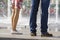 Close up of two pairs of legs, girl in short dress with floral pattern and white shoes and man in blue jeans and brown shoes,stand