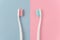 Close up of two plastic white toothbrushes with pink and blue bristle on pink and blue background.