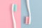 Close up of two plastic white toothbrushes with pink and blue bristle on pink and blue background. Free copy space.