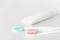 Close up of two plastic white toothbrushes with pink and blue bristle and toothpaste in tube.