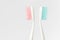 Close up of two plastic white toothbrushes with pink and blue bristle on white background.