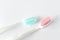 Close up of two plastic white toothbrushes with pink and blue bristle on white background.