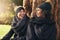 Close-up of two smiling young women leaning on tree trunk in autumnal park