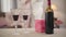 Close-up of two wineglasses and bottle standing on table with gift box. Blurred elegant Caucasian senior couple dancing