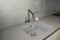 A close-up on undermount enameled cast iron single basin gray kitchen sink with a stainless steel kitchen faucet against gray wall