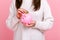 Close up of unknown faceless woman looking at camera, putting coin into piggybank, savings of money.