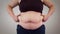 Close-up of unrecognizable Caucasian woman`s tummy. Obese adult woman shaking fat on belly. Overweight, obesity