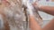 Close-up of unrecognizable female groomer gently washing foot of Labradoodle dog with shampoo in bathtub at grooming