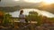 CLOSE UP: Unrecognizable girl and her dog observing lake from above at sunset.