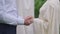 Close-up of unrecognizable Middle Eastern bride putting ring on finger of Caucasian groom standing at altar outdoors