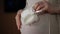 Close-up. An unrecognizable pregnant woman holds white knitted booties in one hand, and gently touching her belly with