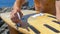 CLOSE UP: Unrecognizable surfer attaching white fins on bottom of his surfboard.