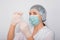 Close-up of a vaccine ampoule in the hands of a woman doctor. Lab technician in a white coat, medical hat, mask and gloves, holds