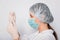 Close-up of a vaccine ampoule in the hands of a woman doctor. Lab technician in a white coat, medical hat, mask and gloves, holds