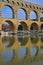 Close up vertical image of three arch level of Pont du Gard with clear reflection on Gardon River
