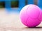 Close-up of a vibrant pink pickleball on a court.