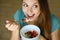 Close up view from above of beautiful young woman eating skyr yogurt with strawberries, cereal muesli and seeds at home, looking