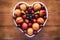 Close-up view from above of a white heart-shaped plate full of red grapes, apricots, strawberry and blueberries. Wooden background