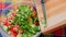 close-up view of adding chopped green onion and dill into glass bowl with cut chinese cabbage, cucumber and red bell