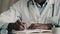 Close up view african man doctor general practitioner medic doing paperwork writing recipe at desk filling checklist