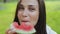 Close-up view of attractive cute brunette young woman with kind eyes, sniffing and eating slice of watermelon and