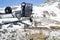 Close up view at back side of snowmobile frame with snow driving black rubber track with supporting wheels, blurry stones and snow