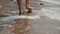 Close-up view of beautiful female feet going forward along the foamy waves of the sea along the sandy shore. Slender and