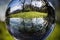 Close up view on beautiful landscape trees in blue sky and green meadow through lens ball sphere, france