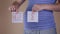 A close-up view of the belly of a pregnant woman in blue who is holding a white sheet of paper with a dollar symbol and