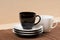 Close up view of black tea cup on the stack of the white and black plates near white tea cup on tablemat.