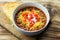 Close up view of a bowl of authentic chili, topped with sour cream, cheese and diced tomatoes, shown with a piece cornbread.