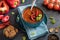 Close up view of a bowl of roasted red pepper soup surrounded by red peppers, crackers and tomatoes.