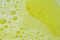 A close-up view of bubbles on yellow washing liquid, creating a bubbly background