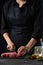 Close-up view of chef cutting with knife meat beef for preparing steak on dark background. Vertical format. Food concept