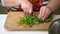 Close up view of chef hands cutting green spinach on wooden cutting board. Making healthy salad at home