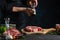 Close-up view of chef pours black pepper on raw steak on wooden chopped board. Backstage of preparing grilled pork meat at