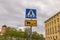 Close up view of crosswalk sign on green trees and grey sky background.