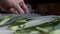 Close up view of cutting green cucumber into small thin slices. Green vegetables preparation in the kitchen