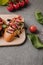 close-up view of delicious bruschetta on wooden board, basil and fresh tomatoes on grey