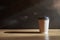 Close-up view of disposable paper glass on wooden table in a sunny cafe.