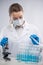 Close-up view of female microbiologist in biohazard protective clothing looking for biological tubes and using microscope.