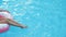 Close-up view of female tanned slender legs lowered in blue refreshing sea pool background, creating waves. The sun rays