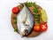 Close up view of fresh Malabar Trevally Fish decorated with curry leaves , tomato,lemon slice and herbs on a white Background