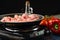 Close-up view of frying pan with raw meat on the stove on dark black background. Backstage of cooking dinner with grilled pork