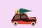 Close up view of glass toy decoration in form of red car figure transporting Christmas tree isolated on pink background
